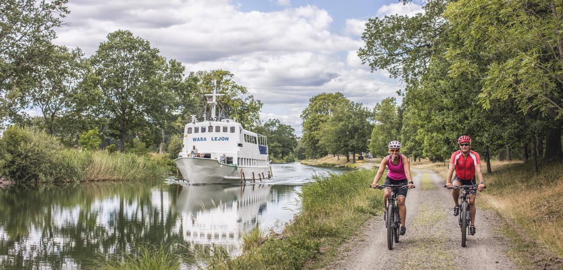 Två cyklar längs Göta kanal, på vattnet en kanalbåt.