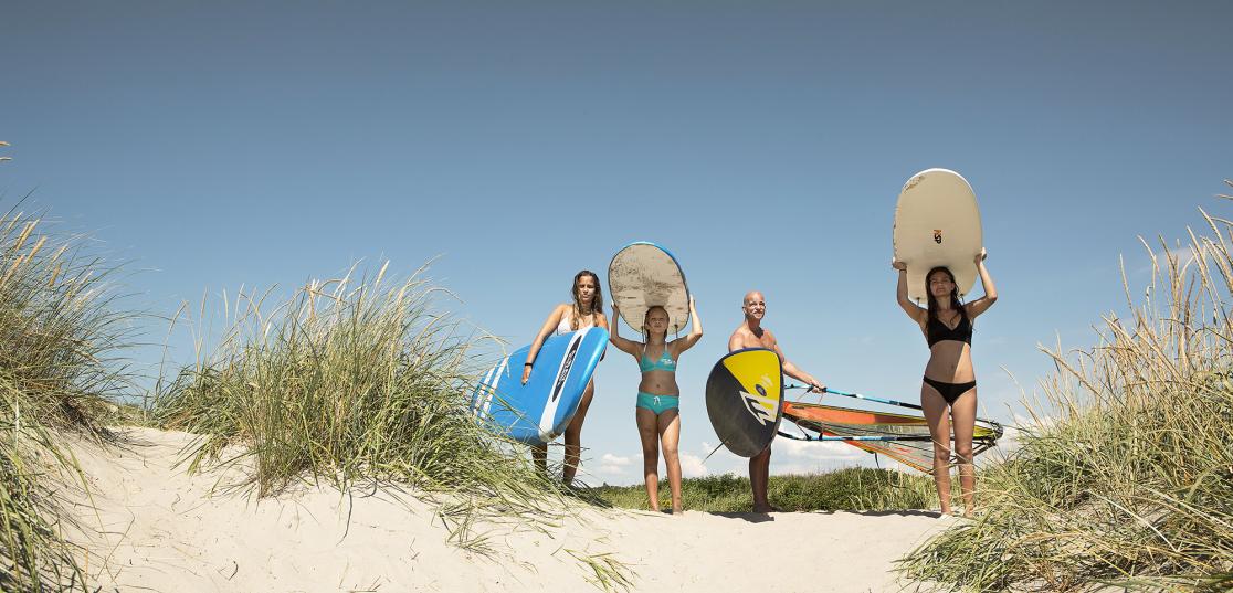 Tre kvinnor och en man med surfingbrädor på sandstrand.