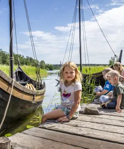 Barn på brygga framför ett vikingaskepp.