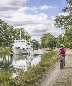 Två cyklar längs Göta kanal, på vattnet en kanalbåt.