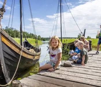 Barn på brygga framför ett vikingaskepp.