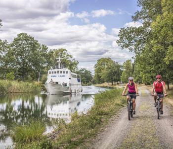 Två cyklar längs Göta kanal, på vattnet en kanalbåt.