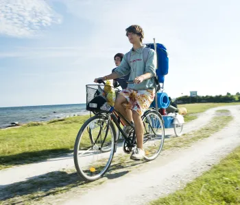 Två personer cyklar på grusväg längs havet.