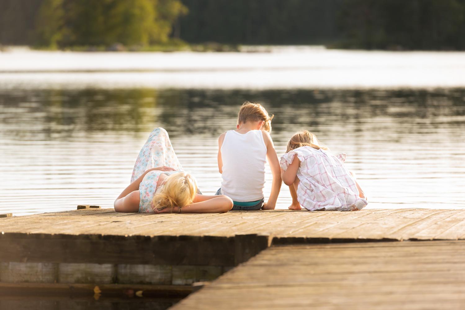 Familj sitter på brygga vid sjö en sommardag.