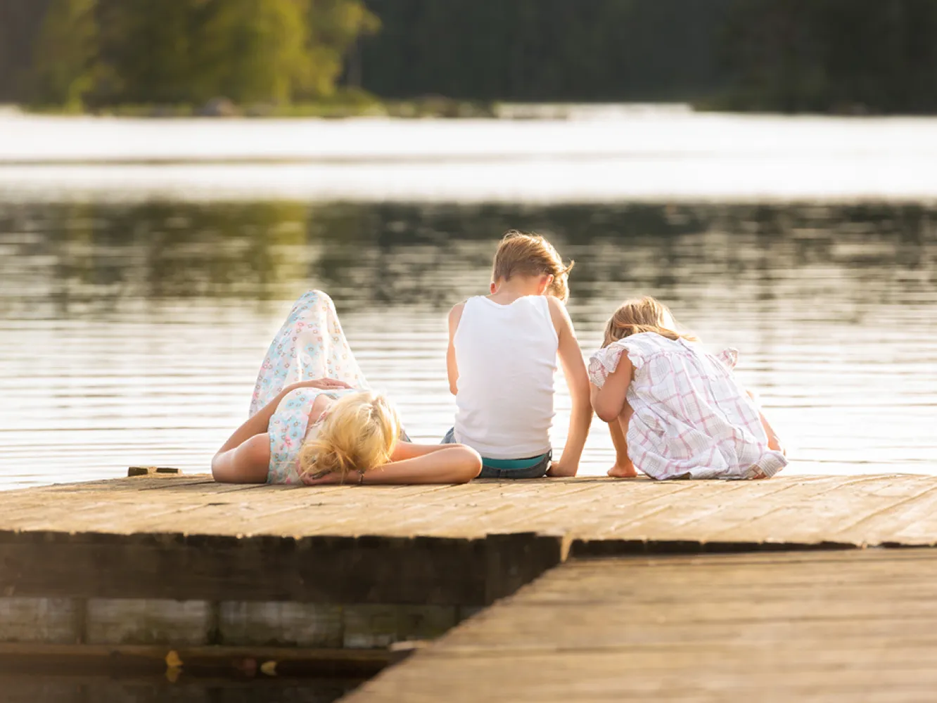 Familj sitter på brygga vid sjö en sommardag.