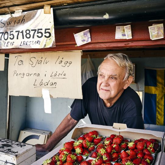 Man i en försäljningsbod med jordgubbar på disken.