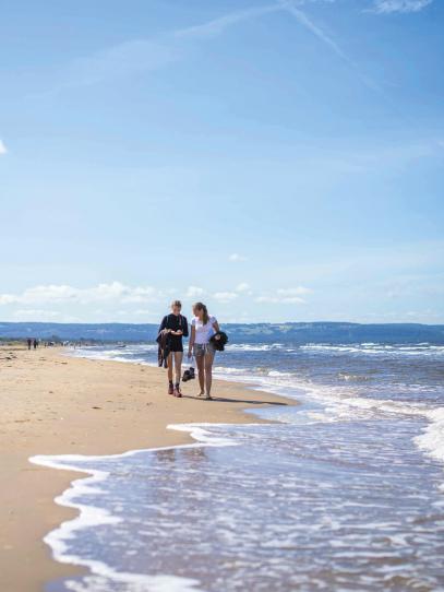 Två personer går längs havet på en vidsträckt strand.