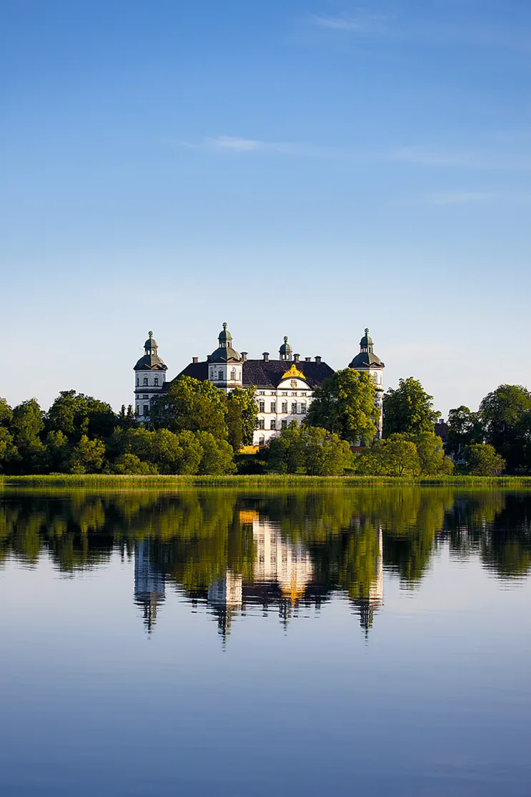 Skokloster inbäddat i gröna träd, speglas i Mälaren.