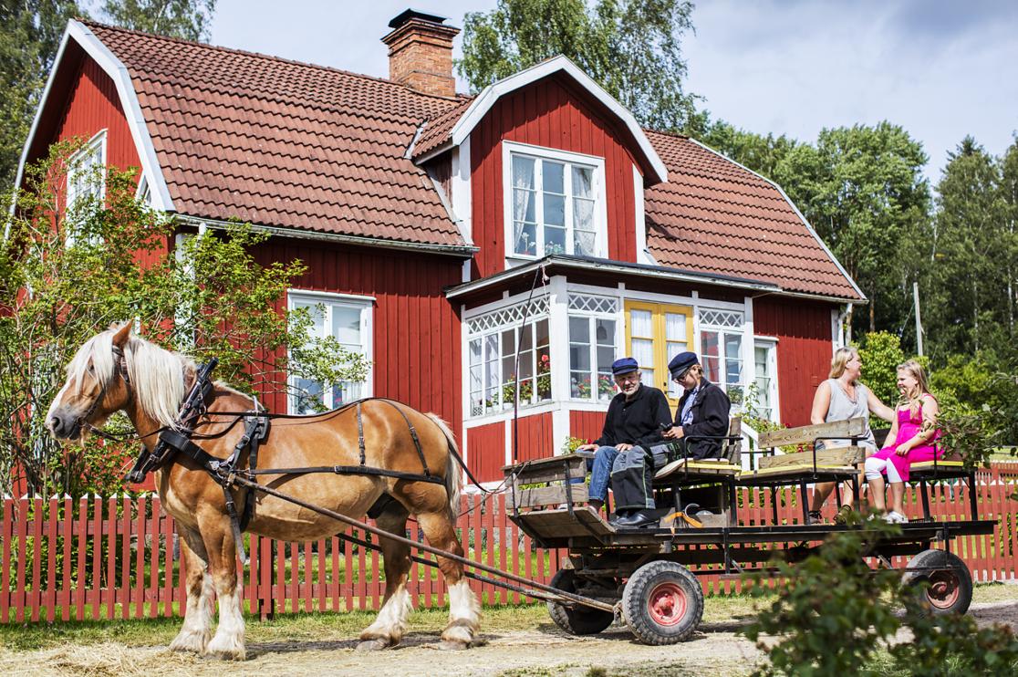 Häst och vagn framför rött hus med vita knutar.