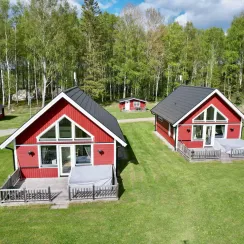 Två röda stugor med altan på en gräsyta omgiven av skog