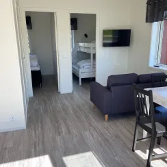 Vardagsrum i stuga med matplats, soffa och sovrum i bakgrunden. 