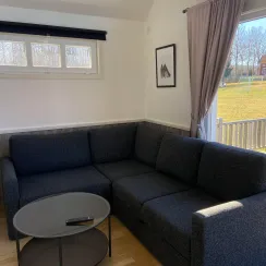 Vardagsrum i stuga med soffa, soffbord och fönster mot uteplats